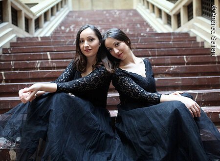 Zwei junge Frauen in schwarzen Abendkleidern sitzen auf einer Treppe.