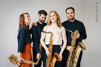 arcis saxophon quartett Eine Gruppe von schwarz gekleideten Personen steht zusammen vor einem hellen Hintergrund. Die Personen halten Saxophone in den Händen.