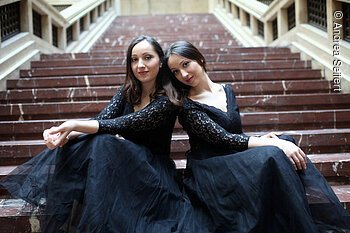 Pianoduo Aninia - Meisterkonzerte 2025 Zwei junge Frauen in schwarzen Abendkleidern sitzen auf einer Treppe.