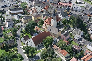 Luftaufnahme einer kleinen Stadt mit Kirche, Wohnhäusern und Straßen, umgeben von Bäumen.