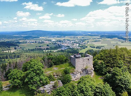 Burgruine Epprechtstein (Kirchenlamitz, Fichtelgebirge) Luftaufnahme einer Burgruine auf einem bewaldeten Hügel mit Blick auf eine ländliche Landschaft und eine Stadt.