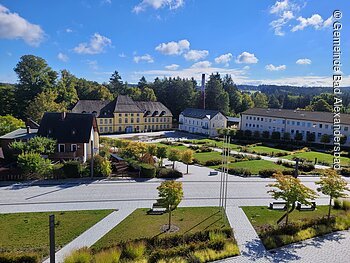 Historisches Gebäude mit gelber Fassade, umgeben von Bäumen und Gärten unter blauem Himmel.