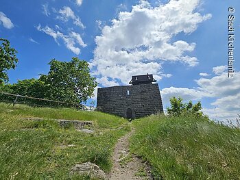 Burgruine Epprechtstein (Kirchenlamitz, Fichtelgebrige) Steinmauer mit Holzdach auf Hügel, umgeben von Bäumen und Wiese, unter blauem Himmel mit Wolken.