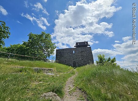 Burgruine Epprechtstein (Kirchenlamitz, Fichtelgebrige) Steinmauer mit Holzdach auf Hügel, umgeben von Bäumen und Wiese, unter blauem Himmel mit Wolken.