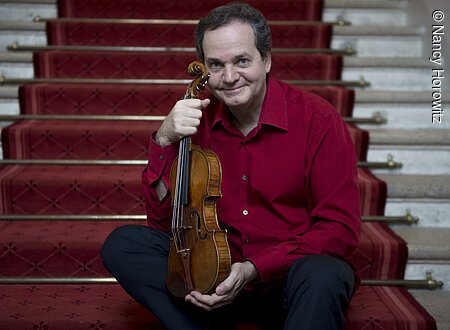 Ein Mann sitzt auf einer Treppe und hält eine Geige vor sich.